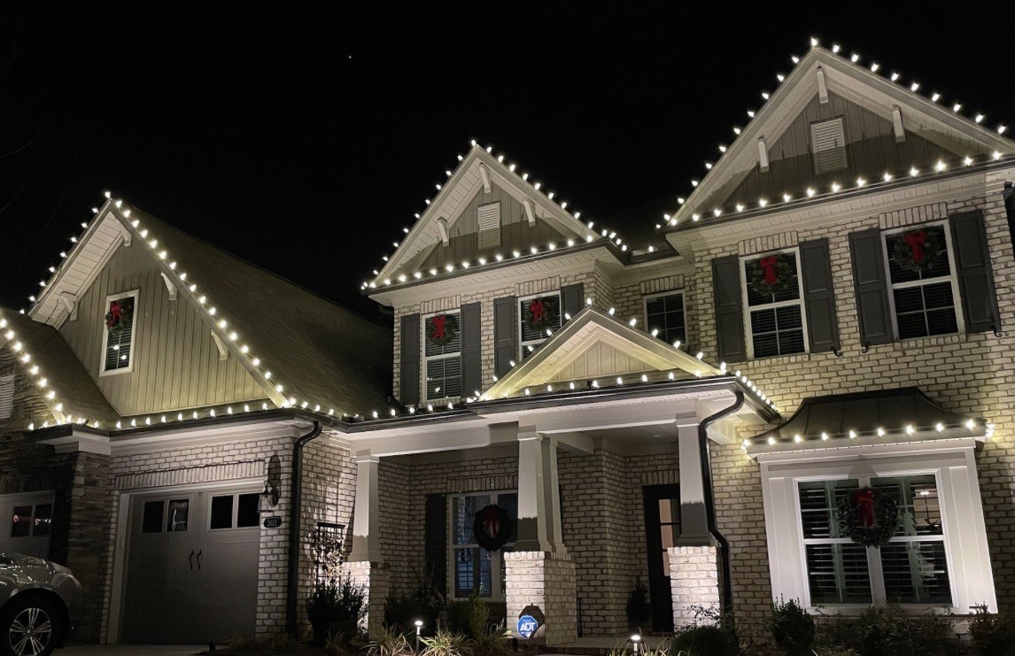 Brick home with custom-cut white holiday lights across multiple roof peaks