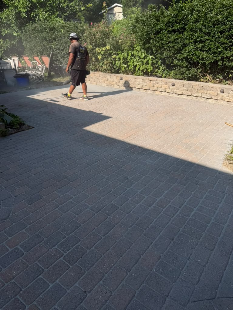 Technician walking a freshly cleaned paver patio with stone wall border