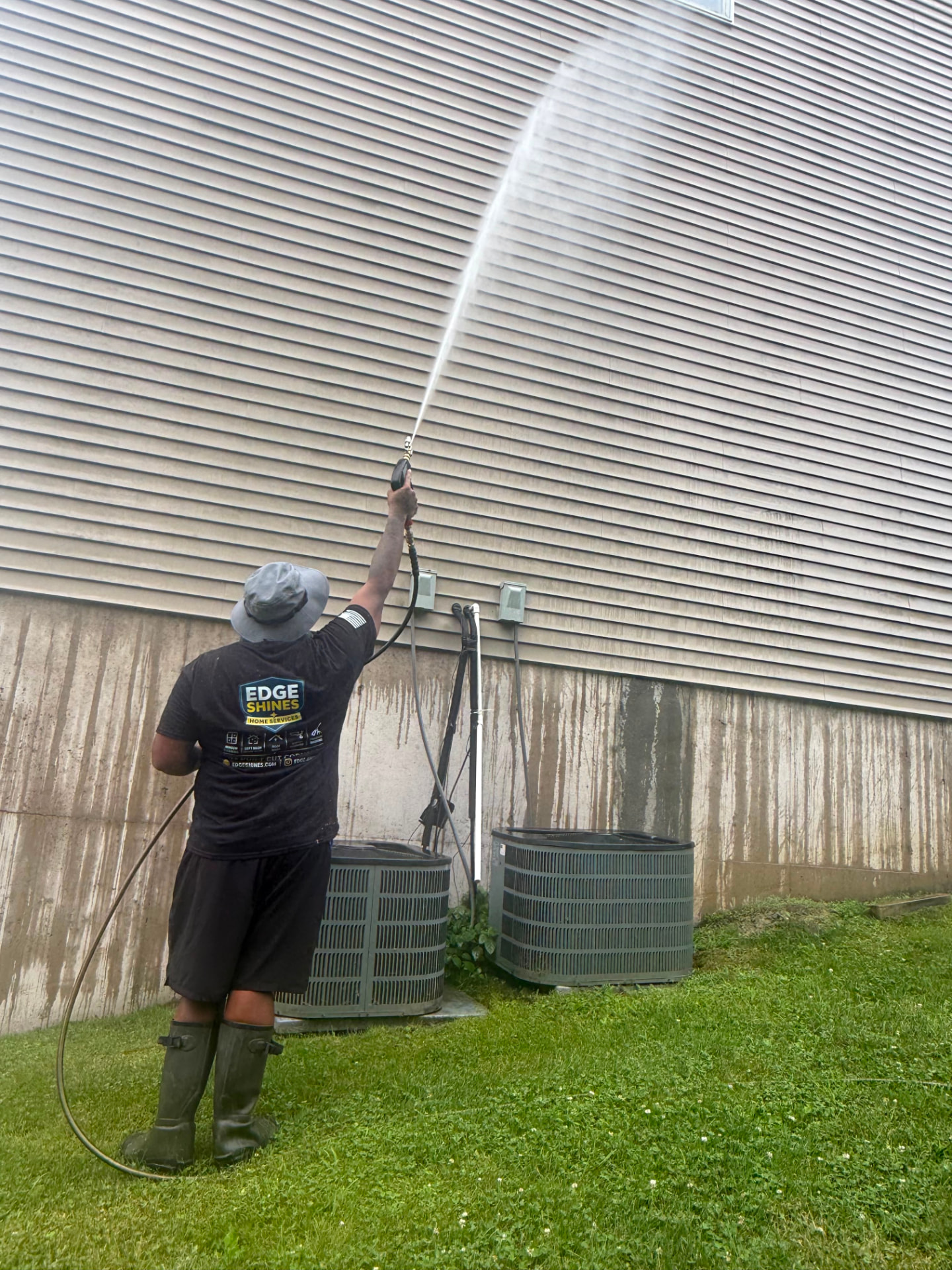 Pressure washing dirty siding on the side of a house