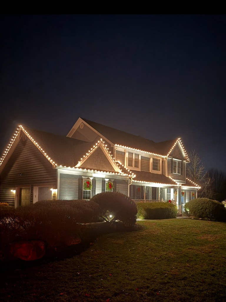 Two-story home decorated with warm white holiday lights and window wreaths