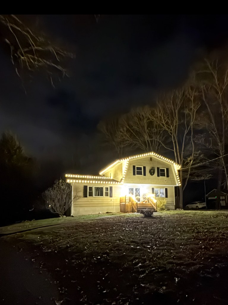 Hudson Valley home glowing with warm white holiday lights along the roofline
