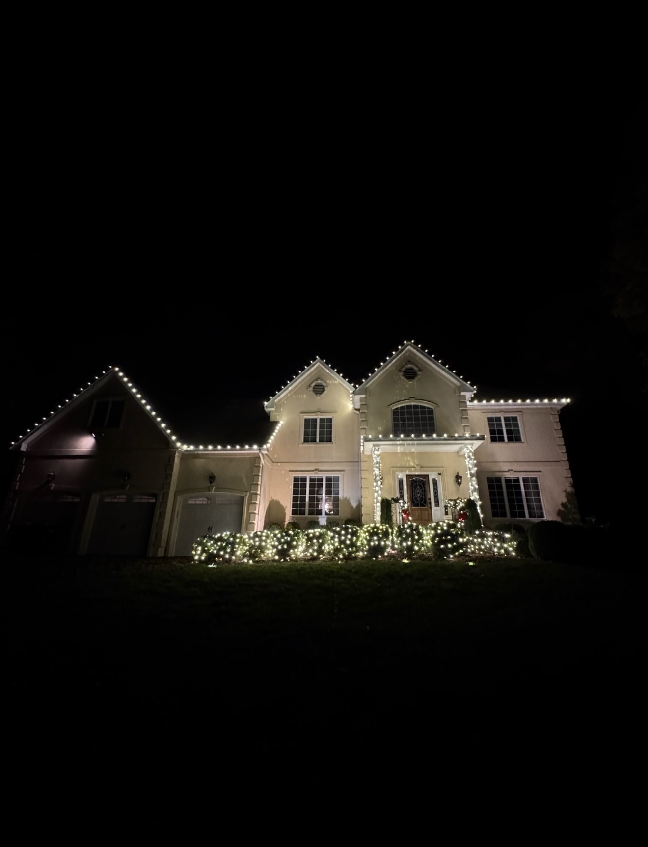 Home and garage outlined in warm white holiday lights with lit foundation hedges